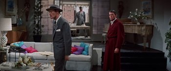 Movie still from “Designing Woman” (1957), directed by Vincente Minnelli – A man in a suit and tie standing next to another man in a red robe; Wide shot, High angle
