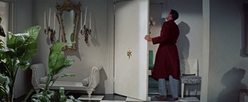 Movie still from “Designing Woman” (1957), directed by Vincente Minnelli – A man in a red coat opening a door to a living room; Wide shot, Low angle