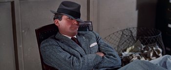 Movie still from “Designing Woman” (1957), directed by Vincente Minnelli – A man wearing a suit and hat sitting in a chair; Close Up shot, Low angle