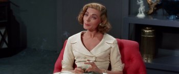 Movie still from “Designing Woman” (1957), directed by Vincente Minnelli – A woman sitting on a red chair holding a cigarette in her mouth; Close Up shot, Low angle