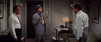 Movie still from “Designing Woman” (1957), directed by Vincente Minnelli – A man wearing a suit and hat standing in a room; Medium shot, High angle