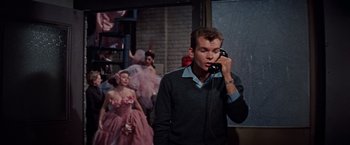 Movie still from “Designing Woman” (1957), directed by Vincente Minnelli – A man talking on a phone in front of a group of women; Medium shot, Low angle