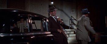 Movie still from “Designing Woman” (1957), directed by Vincente Minnelli – A man in a suit and hat standing next to a car; Medium shot, High angle