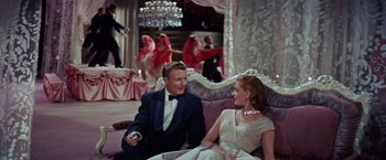 Movie still from “Designing Woman” (1957), directed by Vincente Minnelli – A man and a woman sitting on a couch in a room; Wide shot, High angle