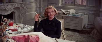 Movie still from “Designing Woman” (1957), directed by Vincente Minnelli – A woman sitting at a table with a pen in her hand; Medium shot, Low angle