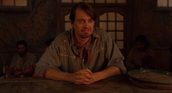Movie still from “Desperado” (1995), directed by Robert Rodriguez – A man sitting at a table with his hands crossed; Medium shot, Low angle