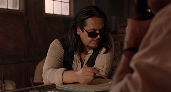 Movie still from “Desperado” (1995), directed by Robert Rodriguez – A man with long black hair is writing on a piece of paper; Medium shot, Over the shoulder angle