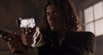 Movie still from “Desperado” (1995), directed by Robert Rodriguez – A man with long hair holding a gun in a dark room; Close Up shot, Low angle