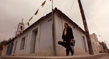 Movie still from “Desperado” (1995), directed by Robert Rodriguez – A man walking down the street holding a skateboard; Wide shot, Low angle