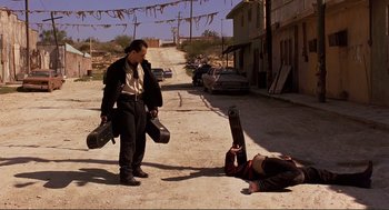 Movie still from “Desperado” (1995), directed by Robert Rodriguez – A man holding a guitar case next to another man laying on the ground; Wide shot, Low angle