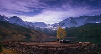 Movie still from “Desperate Hours” (1990), directed by Michael Cimino – A car is parked on the side of the road near a lake; Extreme Wide shot, High angle