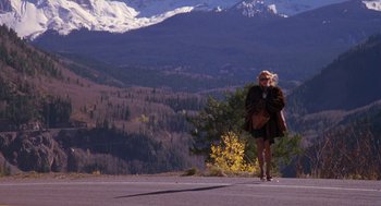 Movie still from “Desperate Hours” (1990), directed by Michael Cimino – A woman standing on the side of a road near a mountain; Extreme Wide shot, High angle