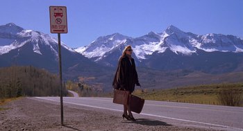 Movie still from “Desperate Hours” (1990), directed by Michael Cimino – A woman walking down the side of a road with a suitcase; Wide shot, Low angle
