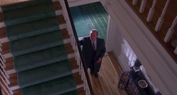 Movie still from “Desperate Hours” (1990), directed by Michael Cimino – A man in a suit standing on the bottom of a staircase; Wide shot, High angle