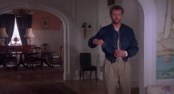 Movie still from “Desperate Hours” (1990), directed by Michael Cimino – A man standing in a living room holding a tie; Medium shot, Over the shoulder angle