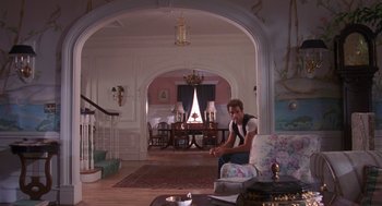 Movie still from “Desperate Hours” (1990), directed by Michael Cimino – A man sitting on a couch in a living room; Wide shot, Low angle