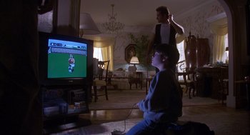 Movie still from “Desperate Hours” (1990), directed by Michael Cimino – A man and a boy are playing a video game; Wide shot, Over the shoulder angle