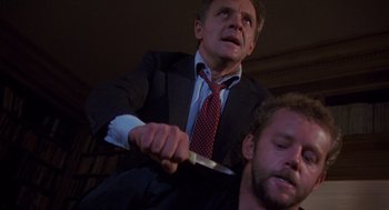 Movie still from “Desperate Hours” (1990), directed by Michael Cimino – A man in a suit and tie cutting another man's hair; Medium shot, Low angle
