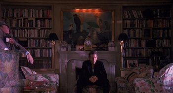 Movie still from “Desperate Hours” (1990), directed by Michael Cimino – A man sitting in front of a fire place in a living room; Wide shot, Low angle