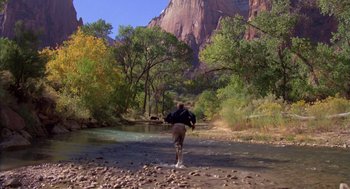 Movie still from “Desperate Hours” (1990), directed by Michael Cimino – A man walking across a river near a forest; Extreme Wide shot, Over the shoulder angle