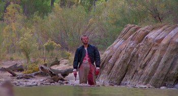 Movie still from “Desperate Hours” (1990), directed by Michael Cimino – A man standing in the water holding a pair of fishing rods; Wide shot, High angle