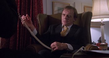 Movie still from “Desperate Hours” (1990), directed by Michael Cimino – A man sitting in a chair holding a phone cord; Medium shot, Low angle