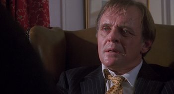 Movie still from “Desperate Hours” (1990), directed by Michael Cimino – An older man wearing a suit and tie sitting on a couch; Close Up shot, Low angle