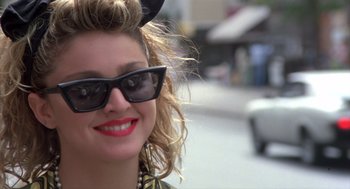 Movie still from “Desperately Seeking Susan” (1985), directed by Susan Seidelman – A person wearing sunglasses on a city street; Close Up shot, Over the shoulder angle
