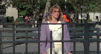 Movie still from “Desperately Seeking Susan” (1985), directed by Susan Seidelman – A woman wearing glasses standing in front of a metal fence; Medium shot, Low angle
