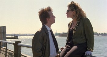 Movie still from “Desperately Seeking Susan” (1985), directed by Susan Seidelman – A man and a woman sitting next to each other on a pier; Medium shot, Over the shoulder angle