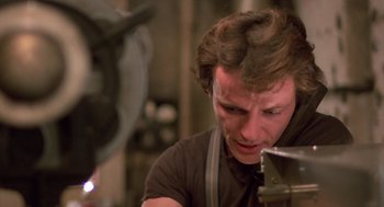 Movie still from “Desperately Seeking Susan” (1985), directed by Susan Seidelman – A man in a brown shirt is looking at a piece of metal; Close Up shot, Low angle