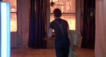 Movie still from “Desperately Seeking Susan” (1985), directed by Susan Seidelman – A man holding a laptop in front of an open window; Wide shot, Low angle