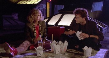 Movie still from “Desperately Seeking Susan” (1985), directed by Susan Seidelman – A couple of people sitting around a table with some food; Medium shot, Low angle