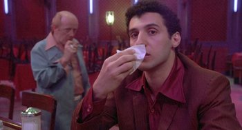 Movie still from “Desperately Seeking Susan” (1985), directed by Susan Seidelman – A man in a red shirt is holding a napkin to his mouth; Close Up shot, Low angle