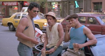 Movie still from “Desperately Seeking Susan” (1985), directed by Susan Seidelman – A group of men sitting next to each other on the street; Medium shot, High angle