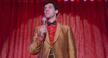 Movie still from “Desperately Seeking Susan” (1985), directed by Susan Seidelman – A man in a brown jacket and a red bow tie holding a microphone; Medium shot, Low angle