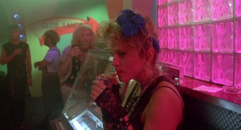 Movie still from “Desperately Seeking Susan” (1985), directed by Susan Seidelman – A woman smoking a cigarette in front of other people; Medium shot, Over the shoulder angle