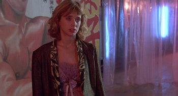 Movie still from “Desperately Seeking Susan” (1985), directed by Susan Seidelman – A woman in a dress and jacket standing in front of a curtain; Medium shot, Over the shoulder angle
