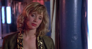 Movie still from “Desperately Seeking Susan” (1985), directed by Susan Seidelman – A woman with blonde curly hair wearing a green and gold jacket; Close Up shot, Over the shoulder angle