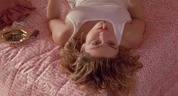 Movie still from “Desperately Seeking Susan” (1985), directed by Susan Seidelman – A woman laying on a bed holding a cell phone to her ear; Close Up shot, Overhead angle