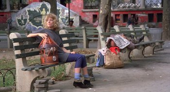 Movie still from “Desperately Seeking Susan” (1985), directed by Susan Seidelman – A woman sitting on top of a wooden park bench; Wide shot, Low angle