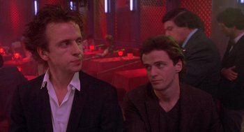 Movie still from “Desperately Seeking Susan” (1985), directed by Susan Seidelman – A couple of men sitting next to each other in a room; Close Up shot, Low angle