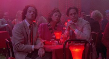 Movie still from “Desperately Seeking Susan” (1985), directed by Susan Seidelman – A group of people sitting at a table in a room; Medium shot, High angle