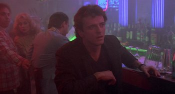 Movie still from “Desperately Seeking Susan” (1985), directed by Susan Seidelman – A man sitting at a table in front of a neon sign; Close Up shot, Low angle