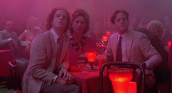 Movie still from “Desperately Seeking Susan” (1985), directed by Susan Seidelman – A group of people sitting at a table in a room; Medium shot, Low angle