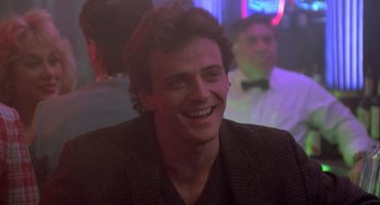 Movie still from “Desperately Seeking Susan” (1985), directed by Susan Seidelman – A young man smiling for the camera at a party; Close Up shot, Low angle