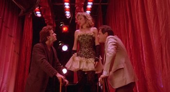 Movie still from “Desperately Seeking Susan” (1985), directed by Susan Seidelman – A group of people standing on a stage with lights in the background; Wide shot, Low angle