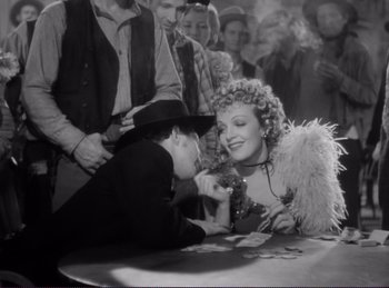 Movie still from “Destry Rides Again” (1939), directed by George Marshall – A man and a woman sitting at a table with other people around them; Medium shot, Over the shoulder angle