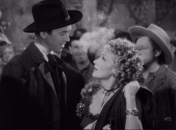 Movie still from “Destry Rides Again” (1939), directed by George Marshall – A man and a woman are standing in front of a group of people; Medium shot, Over the shoulder angle