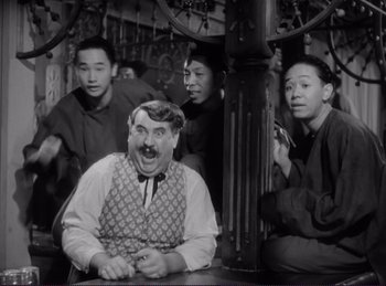 Movie still from “Destry Rides Again” (1939), directed by George Marshall – A man with a mustache sitting in front of a group of people; Medium shot, High angle